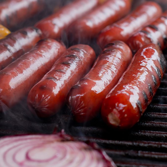 A group of ten Schwab hot links on a hot grill with a sliced onion in the foreground